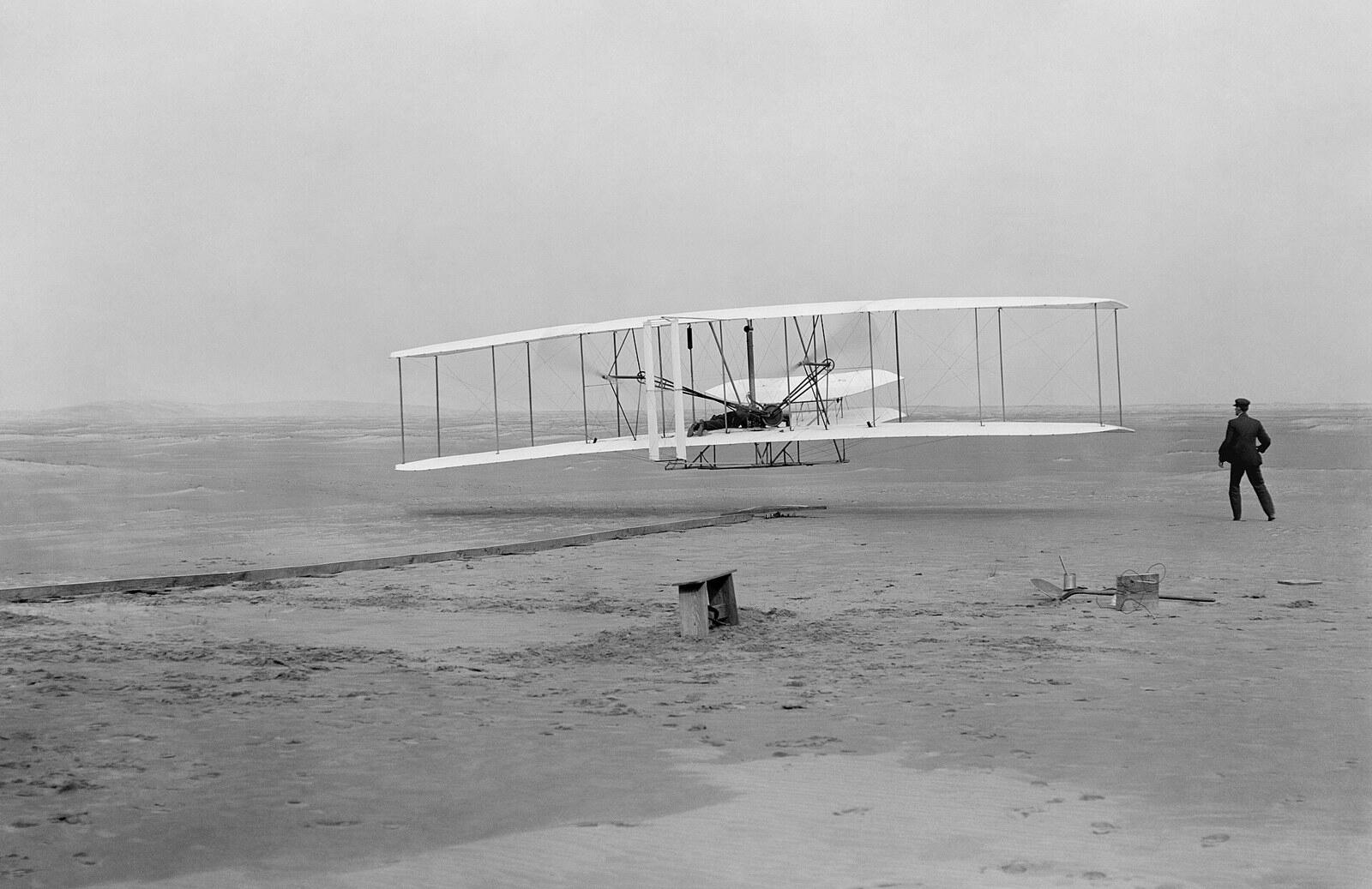 ภาพประวัติศาสตร์ 17 ธันวาคม 1903 เครื่องบิน Wright Flyer ลอยขึ้นจากพื้นทรายเป็นครั้งแรก มีออร์วิลล์บังคับ และวิลเบอร์วิ่งตามอยู่ข้างๆ